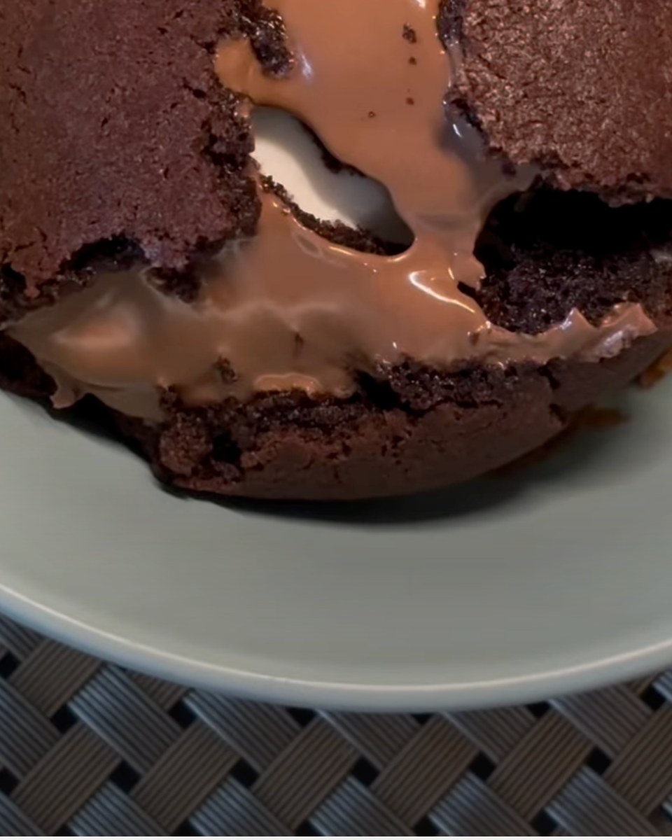 A dark chocolate cookie cut open on a grey plate. Melted milk chocolate and a white filling flow out of the middle across the plate.